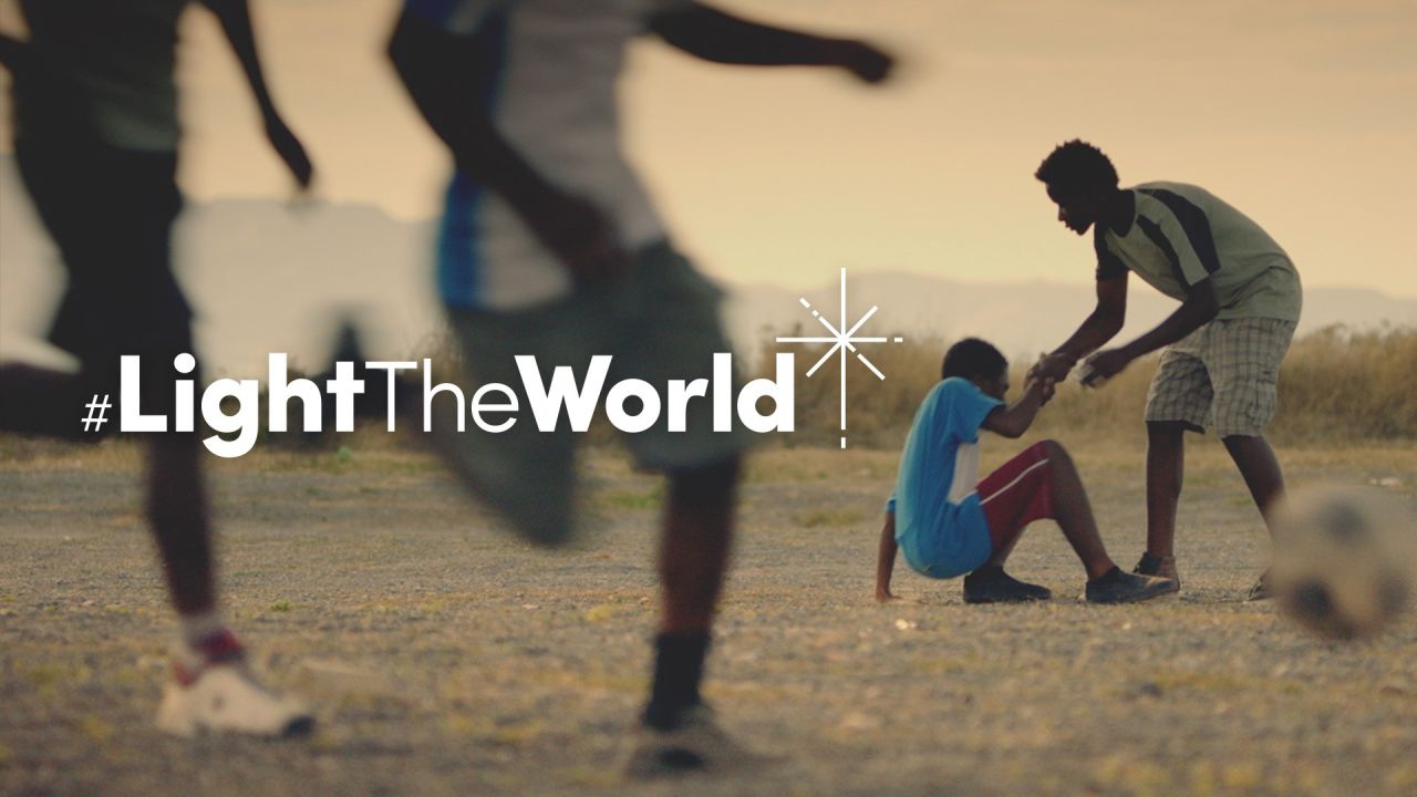 Një djalë ndihmon një djalë tjetër të ngrihet pasi është rrëzuar duke luajtur futboll nga materiali filmik Ndriçoje Botën